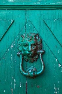 Close-up of rusted lion head shaped metal door knocker on green painted wooden entrance door,