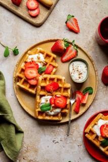 A cozy, rustic setting featuring homemade waffles topped with fresh strawberries and yoghurt. This