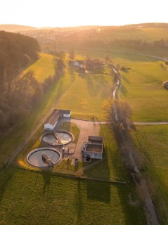 Sewage treatment plant surrounded by green fields and trees, captured at sunset in a quiet rural