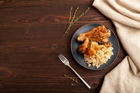 Fried Turkey Wing with spices and thyme on plate on brown wooden background and linen textile. top