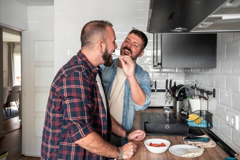A cheerful gay couple shares a lighthearted moment in the kitchen, enjoying each other's company.