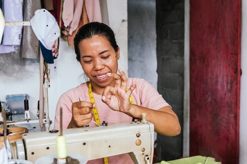A asian seamstress skillfully threads a sewing machine in a cozy workspace. Surrounded by fabrics