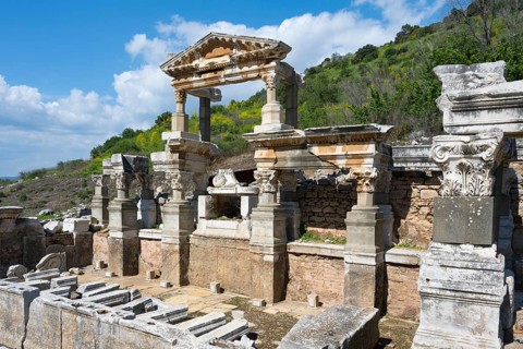 Roman ruins with dominant columns against a green landscape and cloudy sky, Trajan's Fountain,