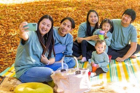 Happy Asian family having a joyful picnic outdoors, sitting on a blanket surrounded by autumn