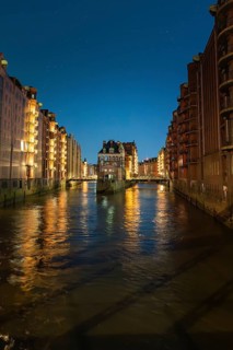 Illuminated canal buildings at night, reflected in the water, under a clear sky, Hamburg, Germany