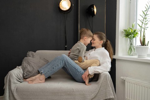 A mother and child share a tender moment, seated on a cozy couch. The room is warm ambiance is