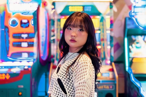 An Asian Gen Z girl enjoys the vibrant and colorful atmosphere of an arcade, surrounded by neon