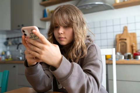 Teen girl in a cozy kitchen setting intensely focused on her smartphone. Dressed casually in a