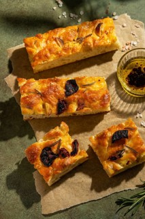 Warm, golden homemade focaccia bread topped with rosemary and garlic, served on parchment. Beside