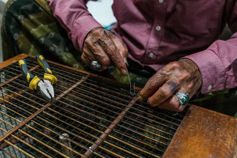 A balinese man skillfully manipulates wire with pliers, showcasing craftsmanship. Their hands,