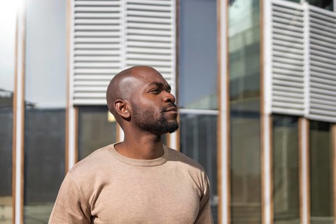 A cuban man in a beige sweater stands confidently outside a modern building with a backdrop of