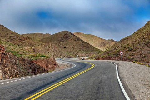 Narrow road leads through a dry, winding mountain landscape, roads through the Quebrada de Cafayate