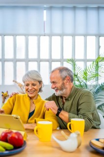 Vertical photo of a caucasian happy mature couple using digital tablet enjoying time together at