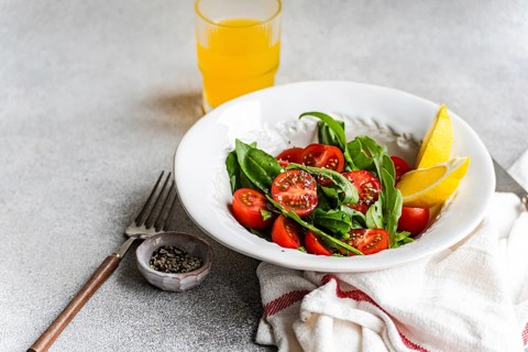 A vibrant salad featuring fresh arugula and herbs, cherry tomatoes, and seeds, drizzled with olive
