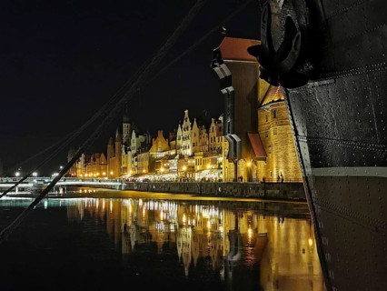 Night view of a ship's bow and illuminated historic buildings on the Motlawa River in Danzig,