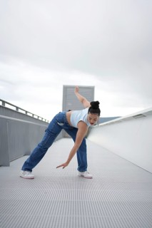 A woman is doing a dance on a white ledge. She is wearing blue jeans and a blue shirt