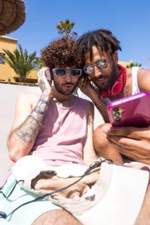 Two men, likely partners, sharing a playful moment looking at a smartphone and listening to music,