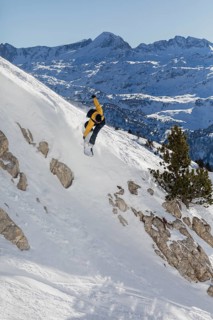 A snowboarder in a dynamic pose navigates a steep, snowy slope against the majestic backdrop of