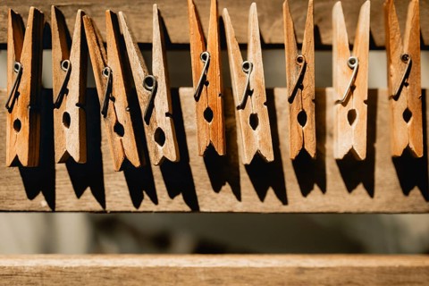 A row of wooden clothespins casting shadows on a rustic clothesline. The warm sunlight highlights