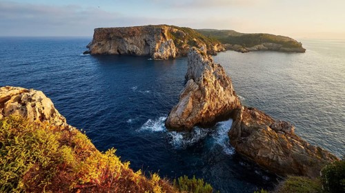 Dramatic cliff landscape surrounded by deep blue sea and waves, morning light, Tsichli Babas islet,
