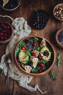 A vibrant salad featuring figs, avocado, cherries, arugula, and blackberries in a wooden bowl. The