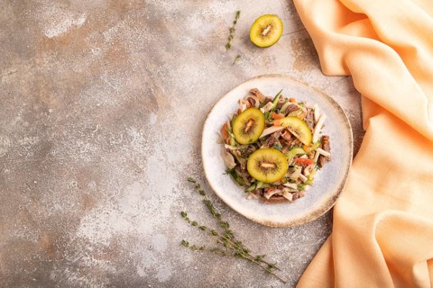 Meat salad with beef kiwi and vegetables on brown concrete background and orange linen textile. top