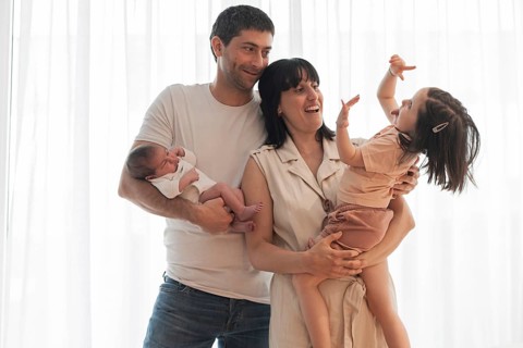 A joyful young family shares a heartwarming moment at home, with parents smiling gently as the big