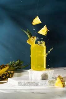 A vibrant pineapple drink in a glass jar with slices of pineapple splashing over it on a marbled