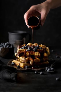 Crop anonymous person adding chocolate syrup from small cup on top of delicious waffles pyramid