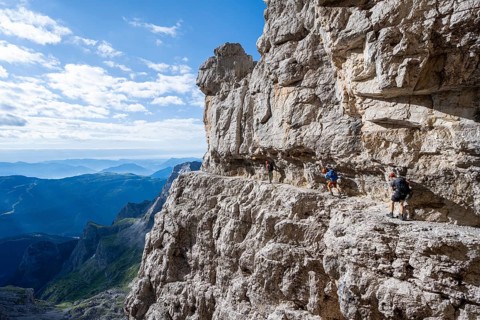 Three mountaineers on an exposed rock band in the secured via ferrata Bocciere Centrale, Brenta
