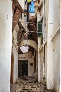 Narrow alleyway with stone steps, flanked by old Mediterranean-style buildings under an overhanging