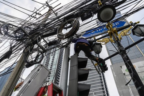 A local Thai engineer working with a tangled web of wires and cables at a set of traffic lights in