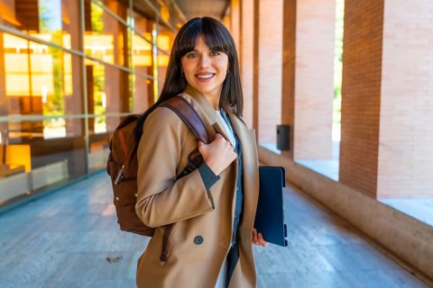 Portrait of a young woman carrying a backpack and tablet, walking through a modern university