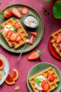 A rustic plate of homemade waffles garnished with fresh strawberries and yoghurt on a vibrant