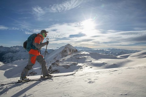 A skier in vibrant gear ascends a snowy mountain under a clear blue sky. The breathtaking winter