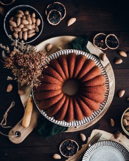 A beautifully baked bundt cake infused with AOVE, almond, and orange sits on a rustic wooden table,