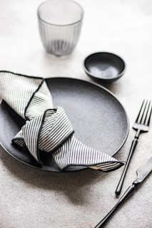 A stylish table setting featuring a black plate, black cutlery, and a striped napkin. The