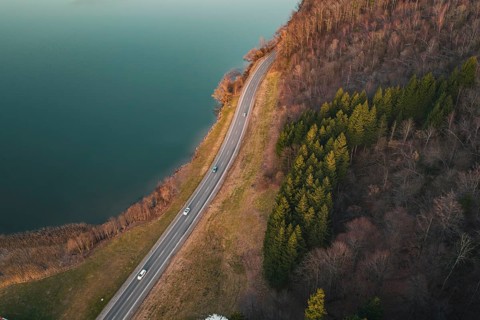 Road with moving traffic along a lake surrounded by dense forest, Großer Alpsee, Immenstadt im
