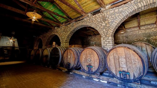 Interior view of a rustic wine cellar with large wooden barrels and vaulted brick ceiling, Achaia