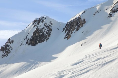 A lone skier ascends a pristine, snowy mountain slope under a clear blue sky, showcasing the serene