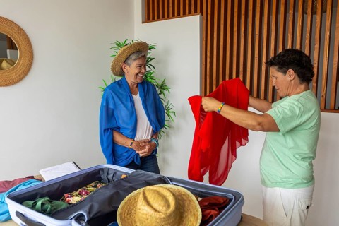 A joyful mature lesbian couple shares a light-hearted moment while packing colorful clothes into a