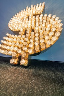 A luminous dollar sign consisting of numerous light bulbs that create a bright, warm glow,