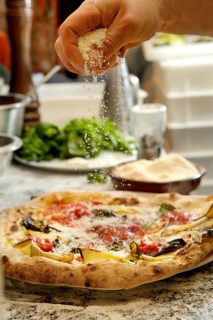 Cropped unrecognizable person sprinkling grated cheese on a freshly baked pizza topped with
