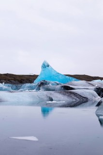 A stunning Icelandic winter scene captures an iceberg's serene reflection in icy waters. The