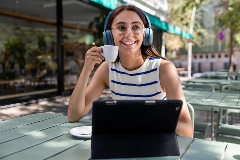 A young woman enjoys a vibrant urban lifestyle, sitting at an outdoor city cafe. With headphones on