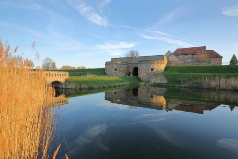 Renaissance moated castle with pond and golden reed grass on the shore, reflection, fortress,