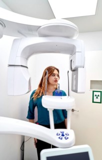 A patient stands inside a dental clinic, positioned for a panoramic X-ray scan. Advanced imaging
