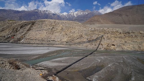 Panoramic view of a river landscape with suspension bridge and mountain backdrop, trekking at