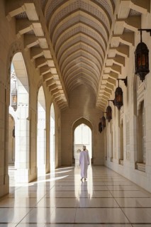 Back view of unrecognizable man in traditional dishdasha Omani attire walkoing along a corridor
