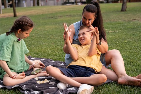 A loving family enjoys a sunny day at the park with their daughter, who has a tracheostomy, and son